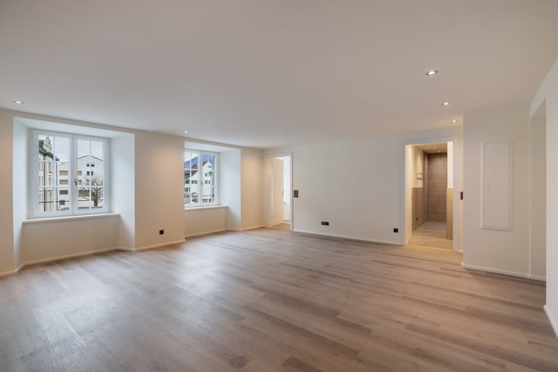Empty room, wooden floors, large windows with views, neutral color scheme, recessed lighting