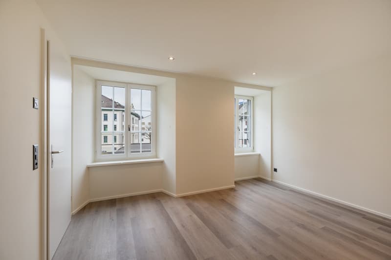 Empty room with wood floors, two windows, and an open door.