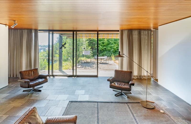 Two leather armchairs, wooden ceiling, tiled floor, large glass sliding doors to balcony, floor lamp