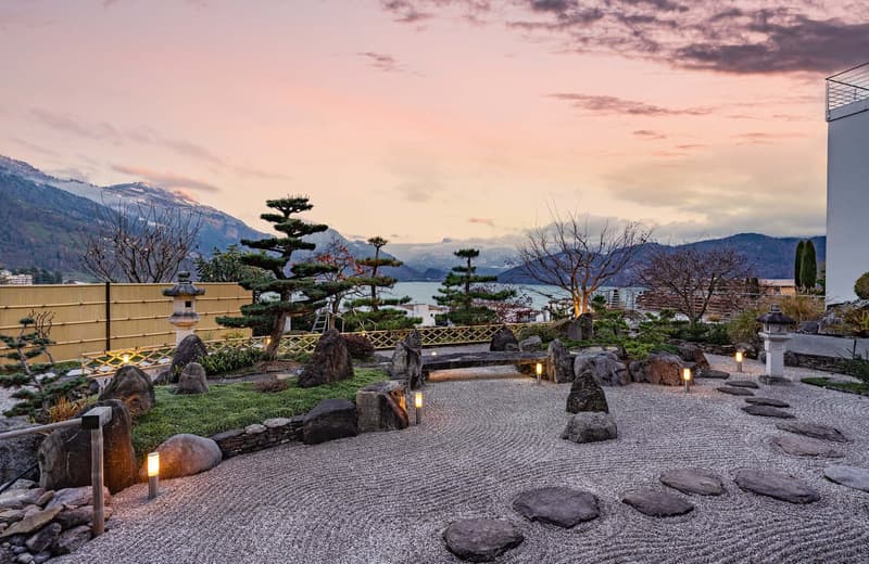 Zen garden with stones, pathway, and landscaping, lanterns, mountains and water in the background