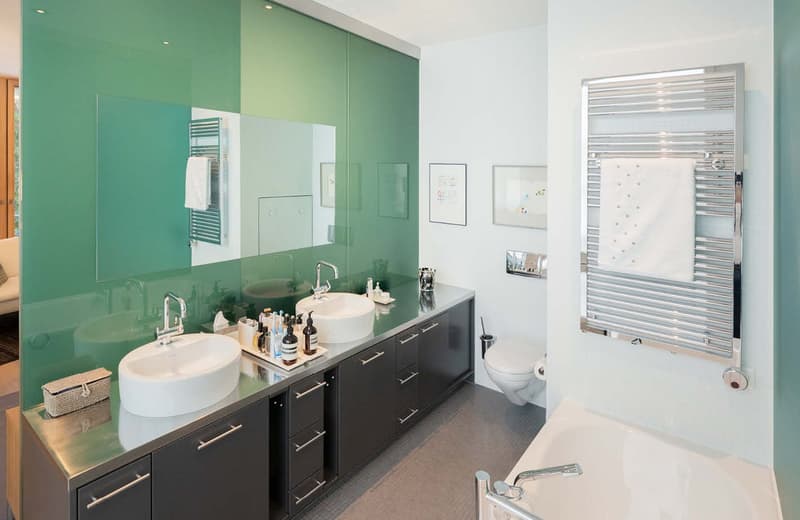 Large bathroom with a double sink, large mirror, a white bathtub, white toilet, and a towel warmer