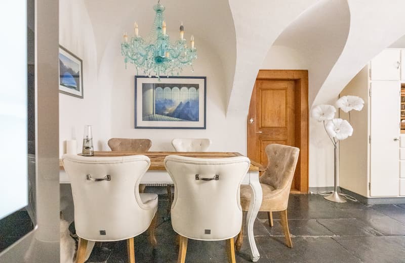 Elegant dining room with a teal blue crystal chandelier, wooden dining table and chairs, framed artwork on the wall, and a wooden door