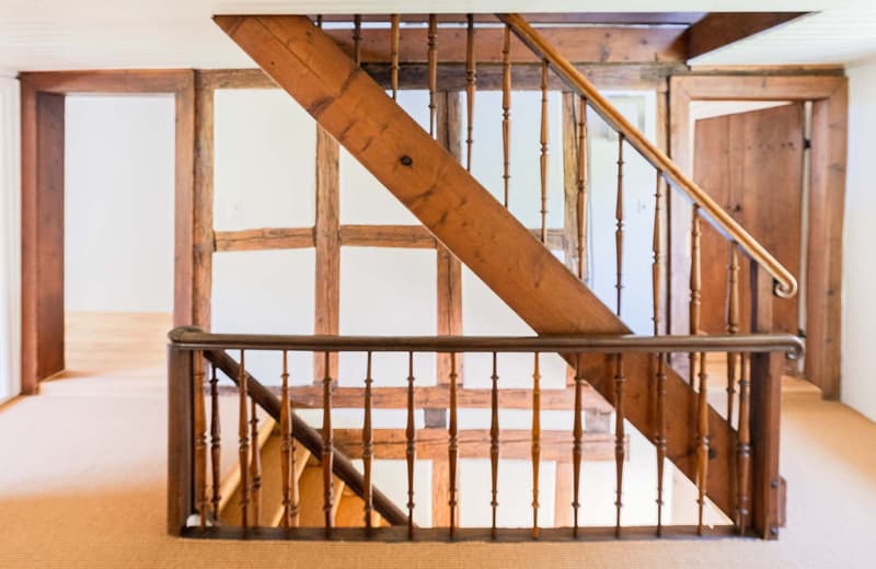 Wooden staircase with spindle railing, exposed wooden beams and framing, hardwood floors