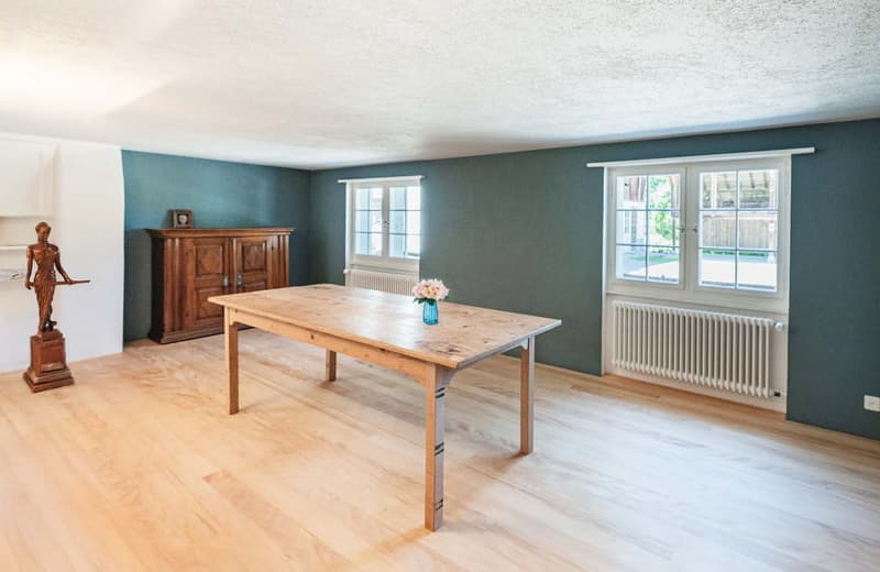 Spacious dining room with wooden dining table, wooden cabinet, and a fireplace. The room has large windows overlooking the outdoor area and hardwood flooring.