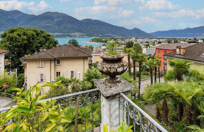 house with multiple floors, balcony, railings, surrounding trees, mountains, and lake