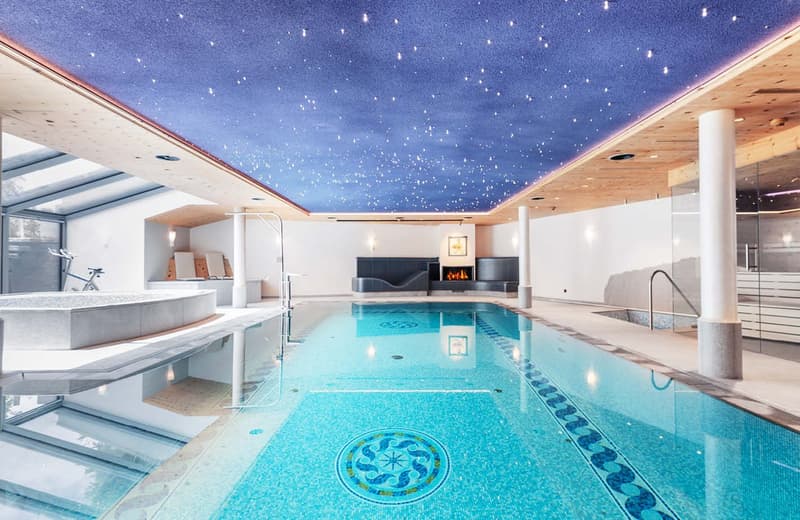 Large indoor swimming pool with a starry night sky ceiling, fireplace, and various amenities such as a bar and seating area.