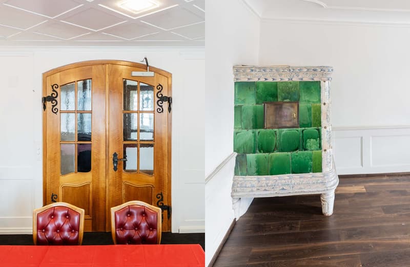 The image shows a room with a wooden arched doorway, red leather chairs, and a large green tiled fireplace or stove in the corner.