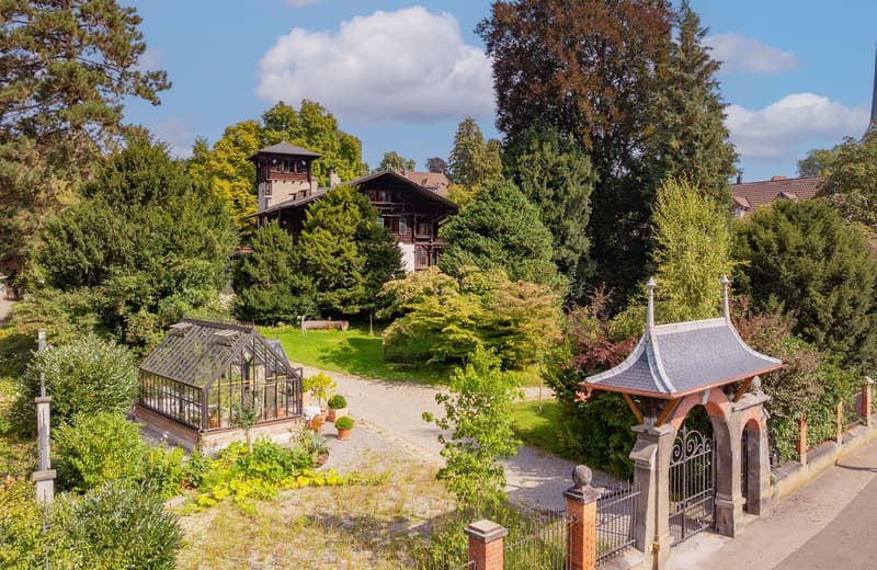 a large house, surrounded by trees and bushes, entrance gate, greenhouse, a pathway to the house, terrace