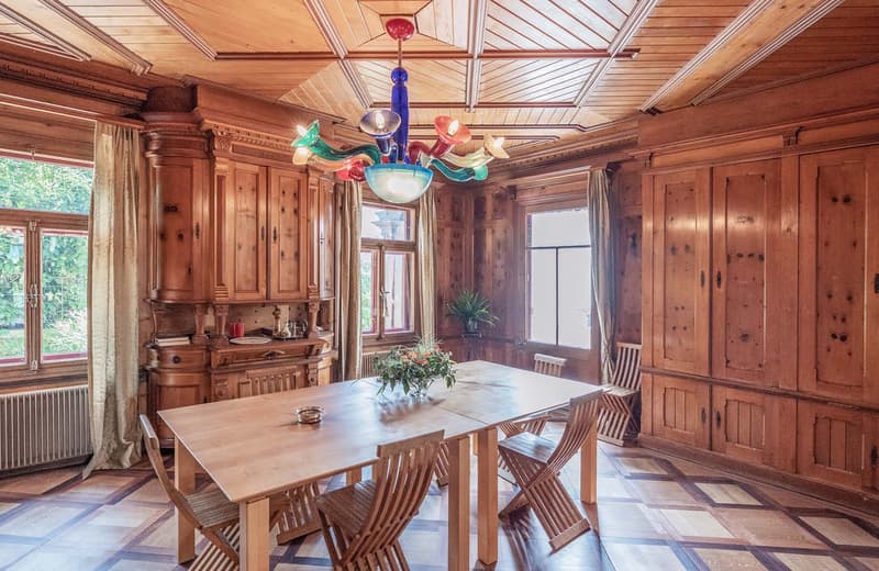 wooden dining table, wooden cabinets, wooden walls, wooden chairs, colorful chandelier, radiator, flower vase