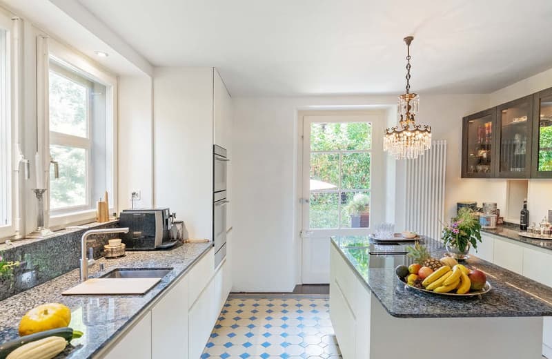 granite countertops, white cabinets, island with breakfast bar, stainless steel oven, microwave, window with natural light, chandelier, white tile flooring, basket of fruits