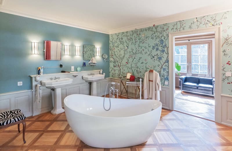 Bathroom: wooden floor, blue walls, freestanding tub, twin vanities, chandelier lights, mirror, hanging towel