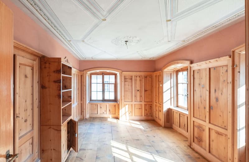 Large, open room with wooden paneled walls and ceiling, arched windows, and a decorative ceiling fixture. The room has a spacious, bright, and rustic feel with the natural wood elements.