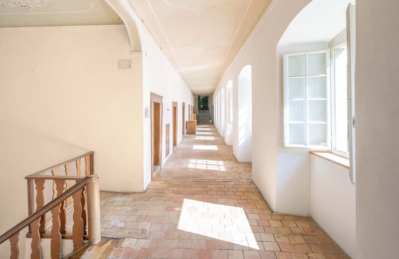 long corridor, white walls, brick floor, arched ceiling, doors, windows, wooden railing