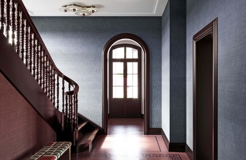Wooden staircase with handrail, patterned tiles at the bottom, arched window, wooden door, and decorative ceiling light