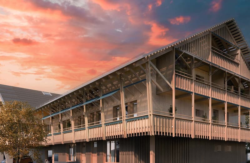 A multi-story wooden building with a large balcony or terrace running along the front, set against a dramatic sunset sky with orange and pink clouds.