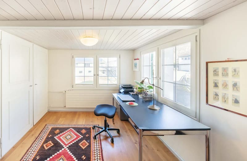 wooden floor, white walls, desk, chair, rug, windows, radiator, ceiling lamp, framed pictures