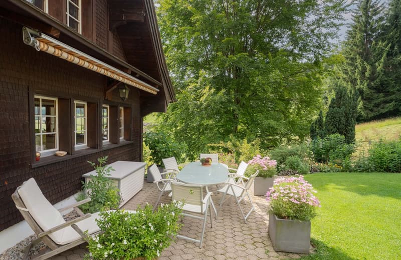 wooden house, gable roof, garden, table and chairs, plants, grass, windows, awning, potted flowers