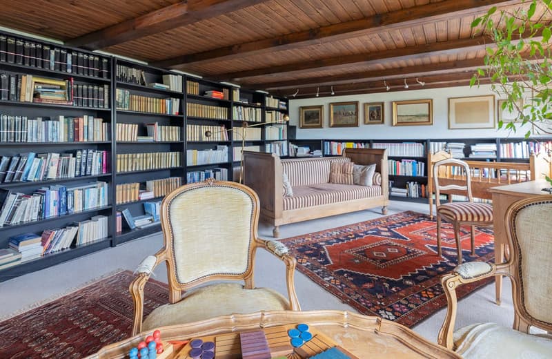 study with a wooden desk, armchairs, bookshelves, a sofa, a rug, and framed pictures