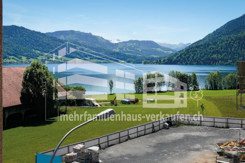 Outdoor scene with a house, lake, mountains, trees, grass, and machinery vehicles