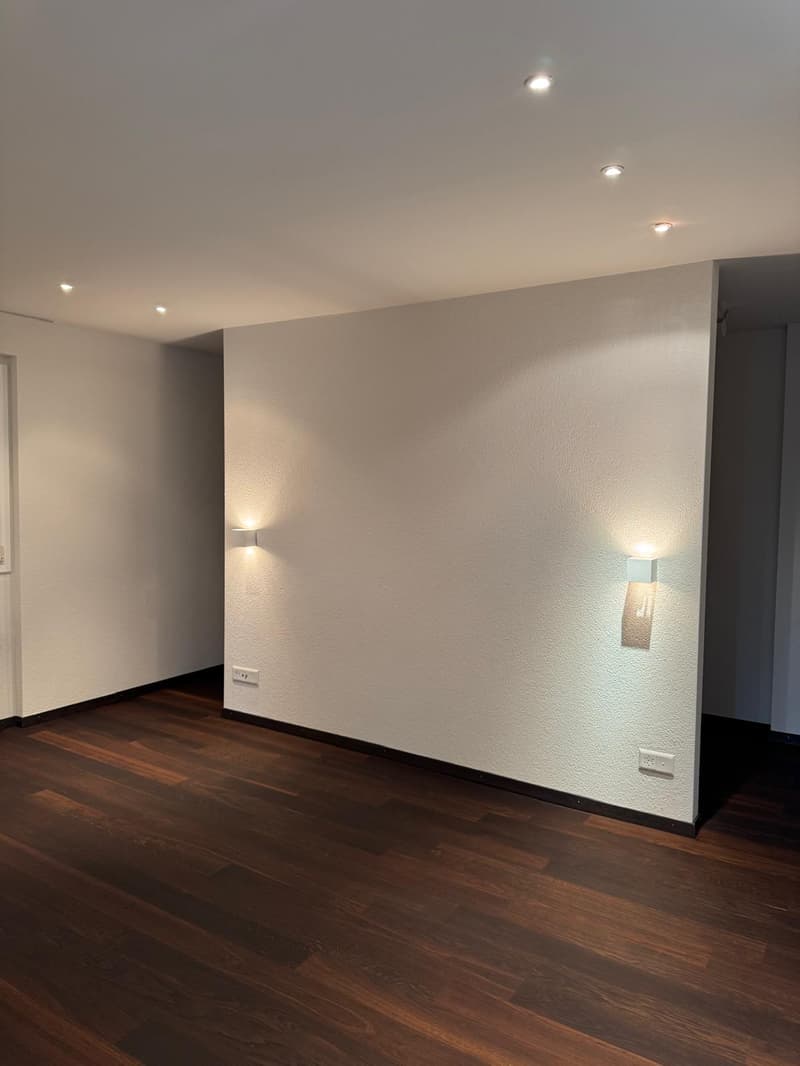 Empty room with white walls, wooden floor, wall-mounted lights