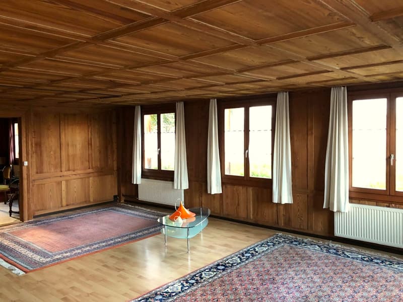 wooden walls, wooden floor, large windows, radiators, two rugs, glass coffee table