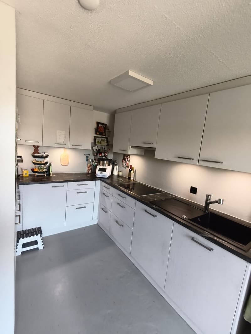 modern kitchen with white cabinets, black countertops, integrated appliances, and ample storage