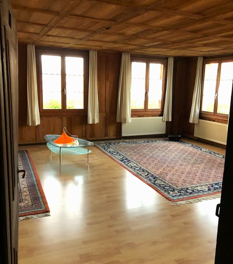 empty room, wooden floor, large windows, wooden wall, two rugs, glass table