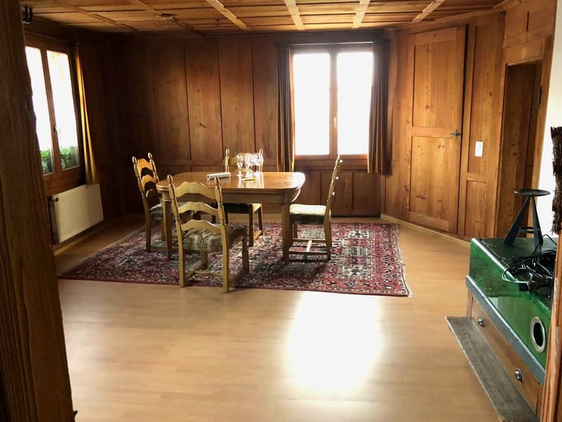 Dining room with wooden walls, wooden floor, dining table, chairs, rug, radiator, windows with curtains