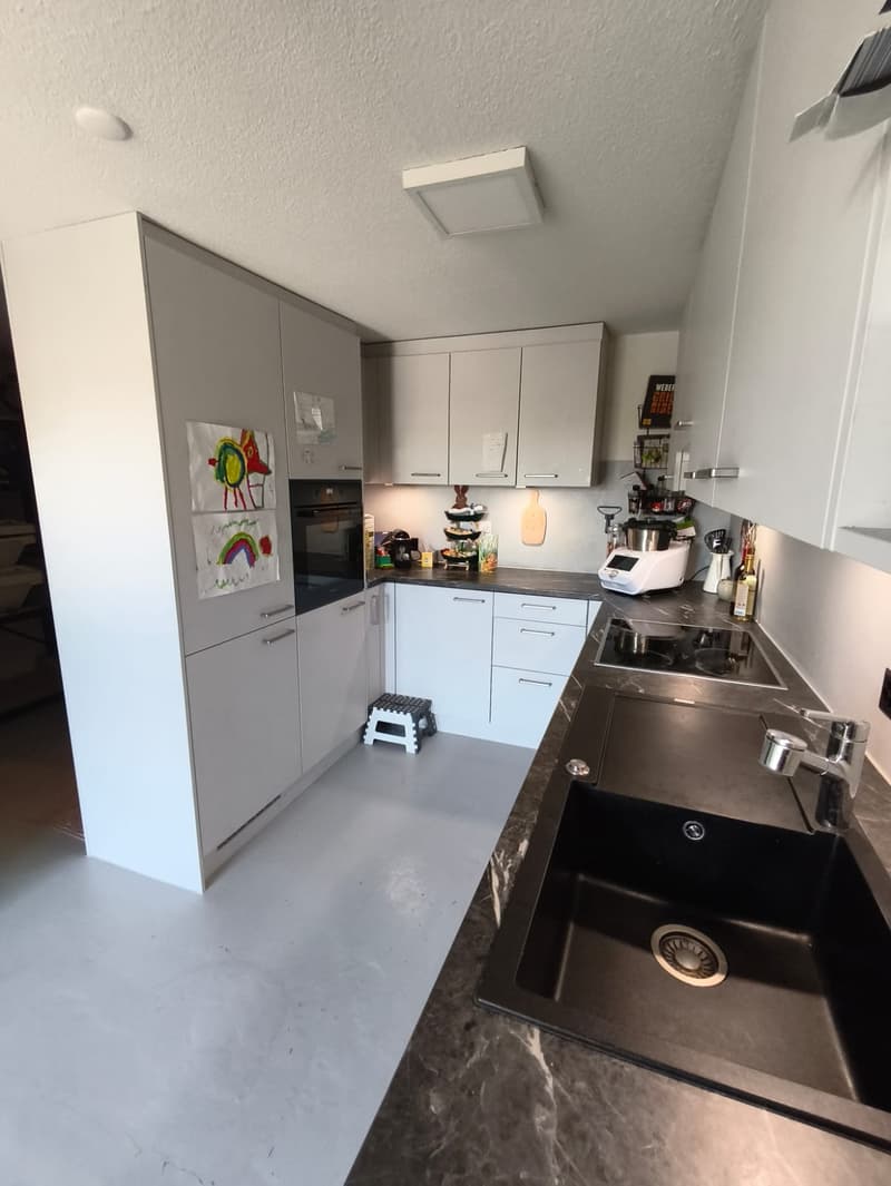 modern kitchen with white cabinets, black countertops, double sink, oven, dishwasher, washing machine, and various kitchen appliances