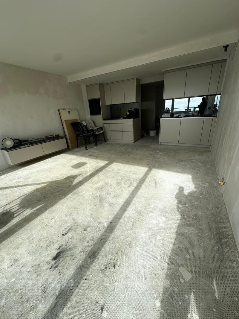 Empty room with white walls, concrete floor, cabinets, chairs, and a table with tools