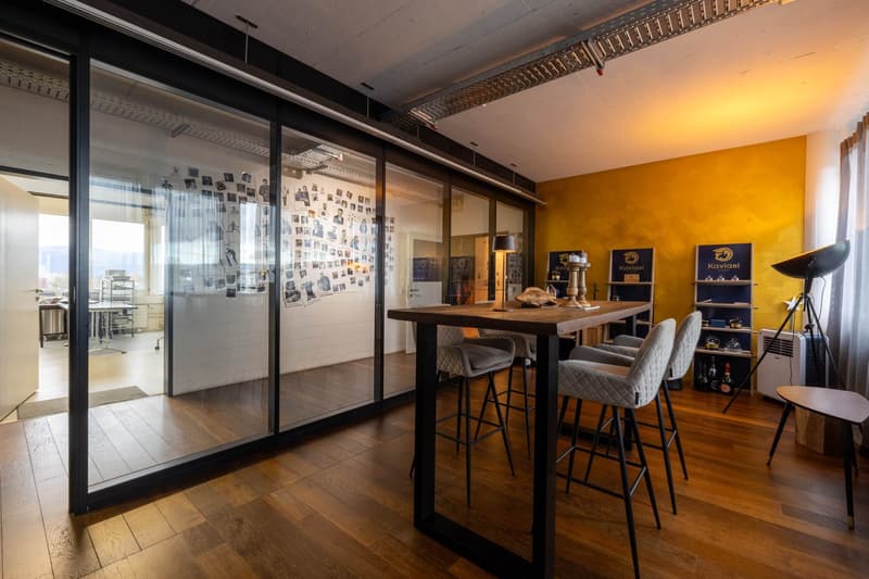modern office room with wooden floor, glass walls, table with chairs, yellow wall, shelves with bottles, lamp, and tripod