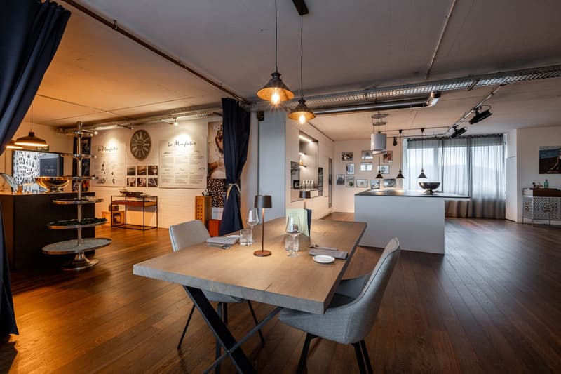 Dining area with wooden floor, modern table, chairs, pendant lights, kitchen area, and decorative items.