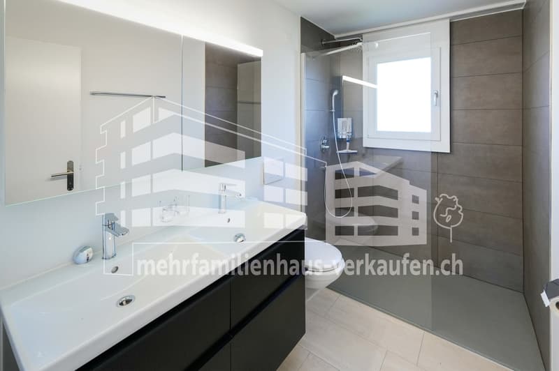 modern bathroom with white sink, black cabinets, glass shower enclosure, toilet, and a window