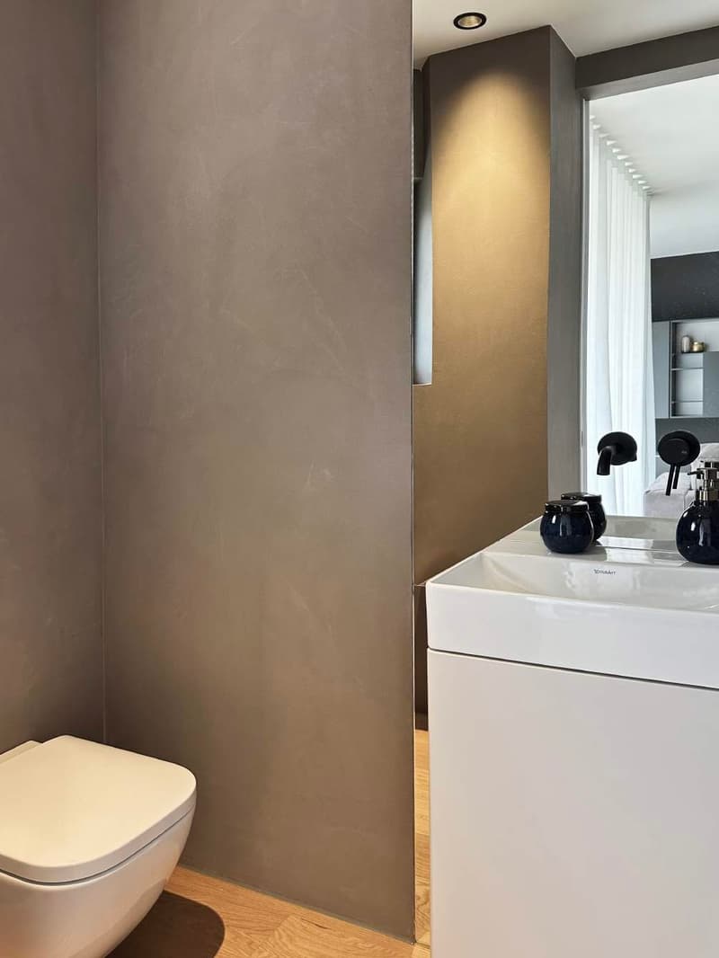 Bathroom with a white wall, toilet, sink and faucets, and a mirror.