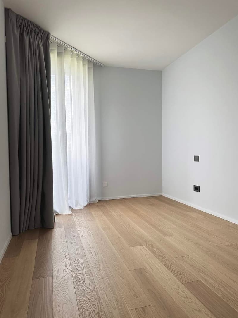 Empty room with wooden floor, white walls, white curtains, power outlets.