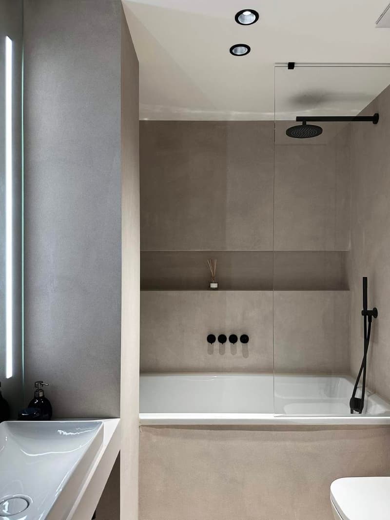 Minimalist bathroom with gray walls, glass shower enclosure, a white bathtub, a white sink, and a white toilet.