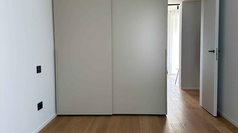 Empty hallway with double doors, wooden floors, and white walls