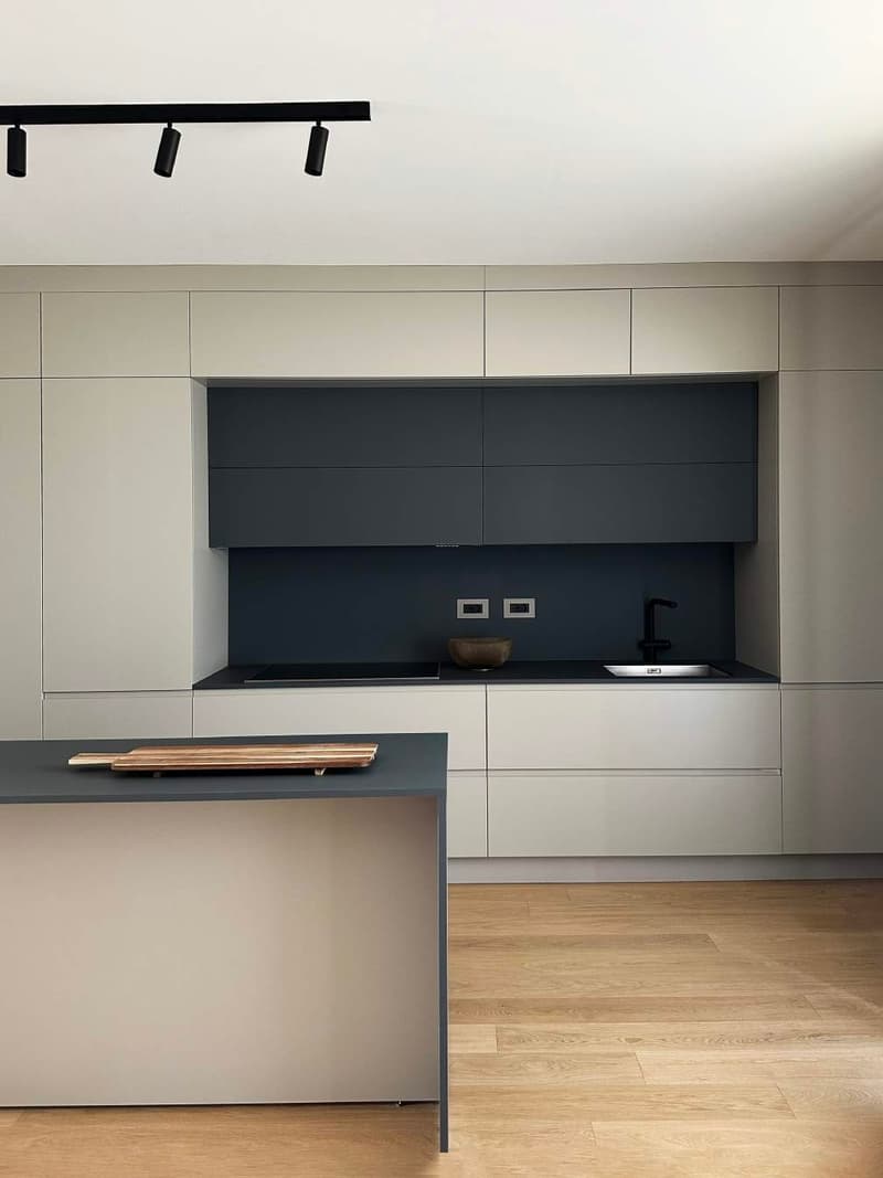 Modern kitchen, white cabinets, dark gray countertops, ceiling lights, wooden floors