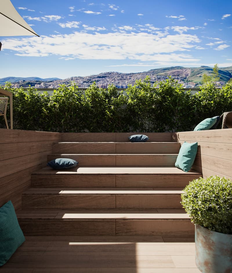wooden deck, outdoor seating area, green shrubs, distant city view