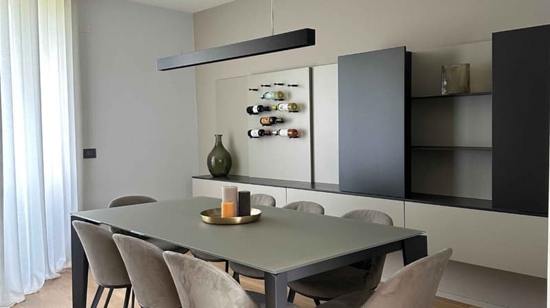 Dining area with gray dining table, gray upholstered chairs, black cabinets, wine rack, white curtains, and a ceiling light