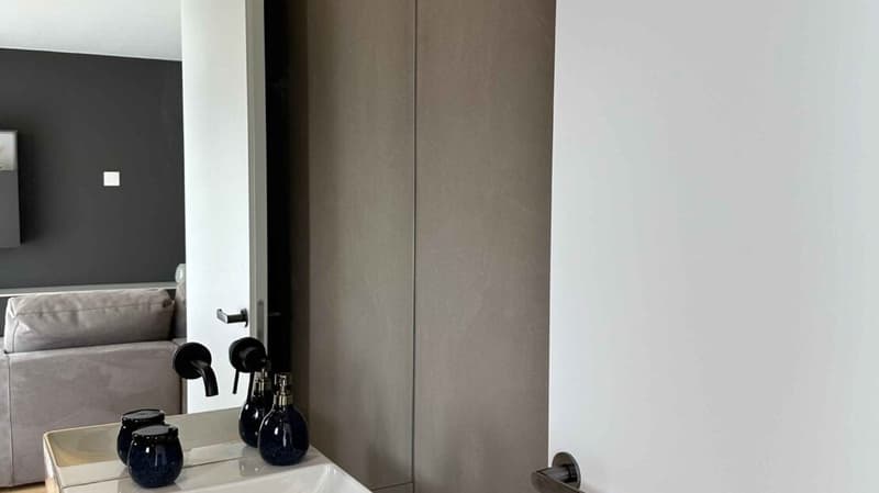 gray walls, white tile floor, white sink, blue bottles on sink, gray couch in background