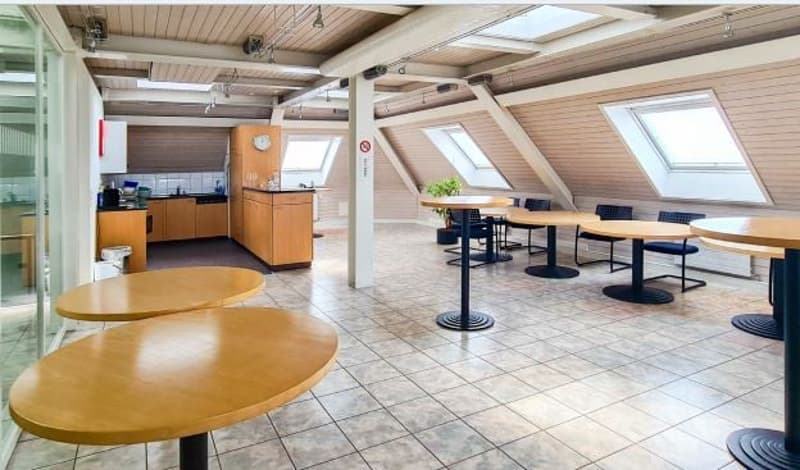 Open space with wooden tables and chairs, kitchen area with wooden cabinets, ceiling with wooden beams and glass windows