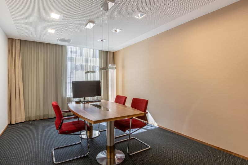 modern office room with table, three chairs, computer monitor, beige walls, curtain, and modern lighting