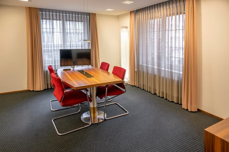 wooden desk, red chairs, mounted television, carpeted floor, vertical curtains