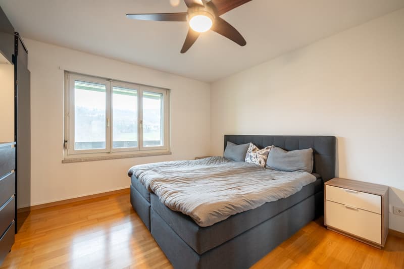Double bed, gray duvet, pillows, wooden cabinet, double window, ceiling fan, power outlet
