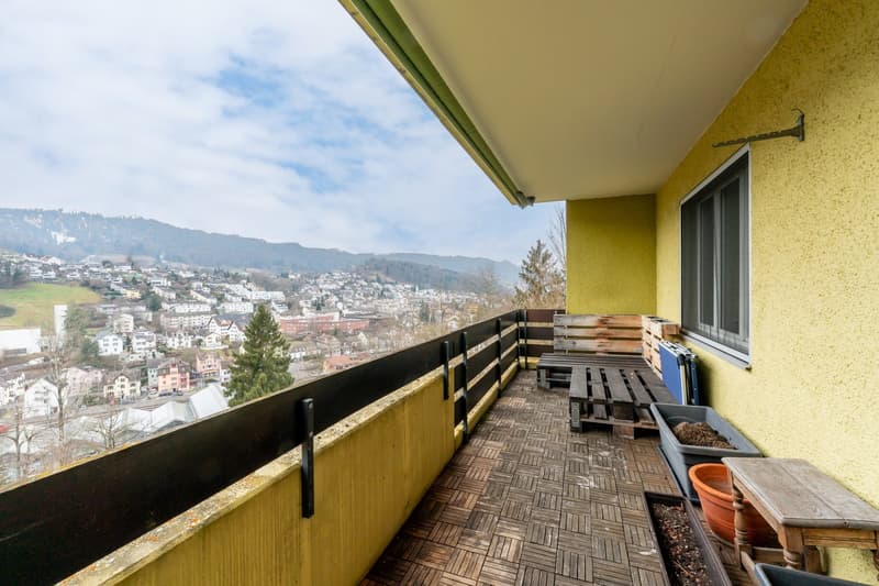 Balcony with wooden flooring, yellow walls, wooden pallet benches, planters, railing, mountain view