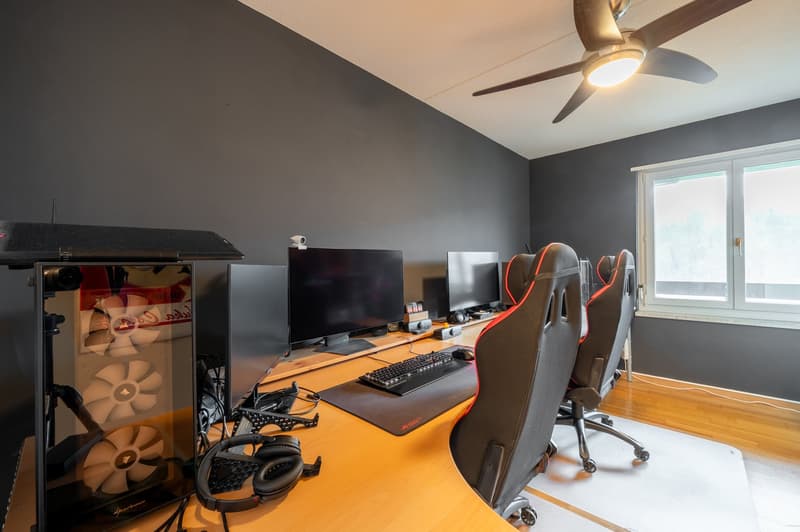 A gaming setup with two monitors, a keyboard, mouse, gaming chair, and gaming equipment on a wooden desk.