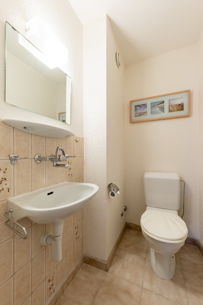 tiled wall, white sink, mirror, mounted frame with photos, toilet