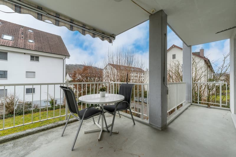 White tiled floor, metal railing, round white table, two grey chairs, white awning, view of green grass