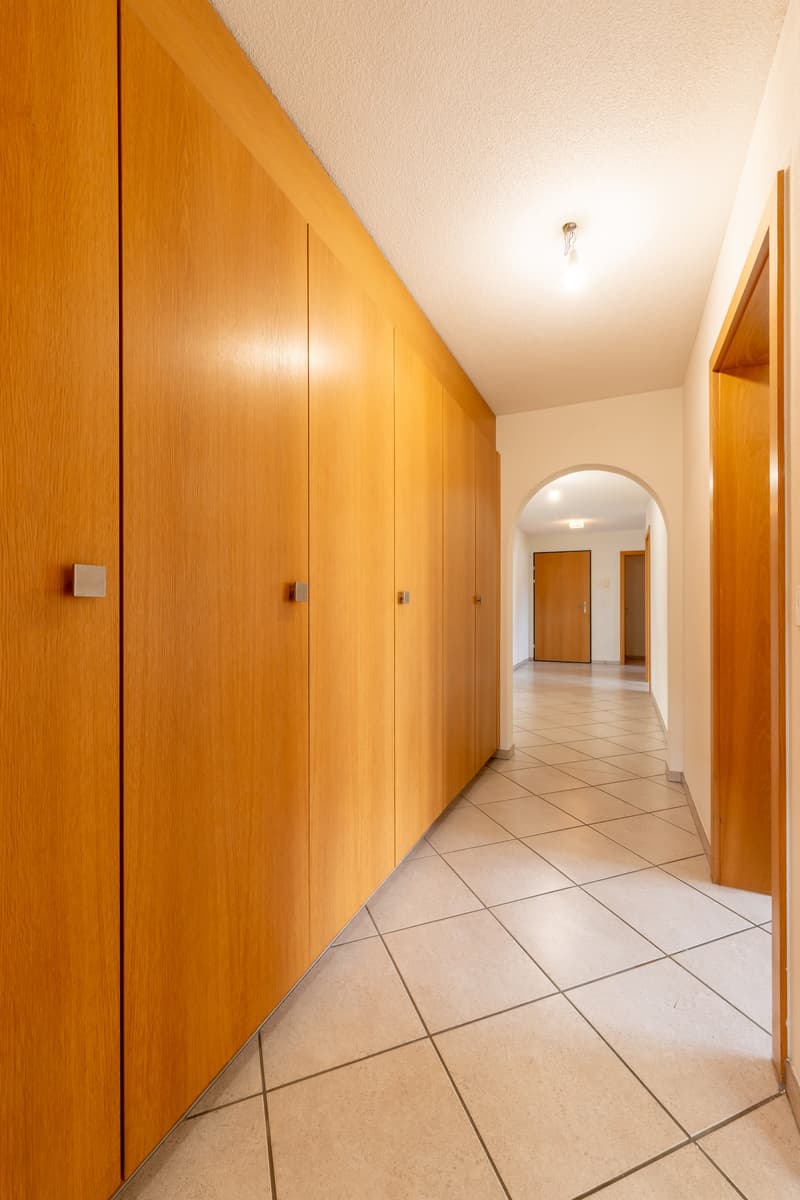 Empty hallway with wooden cabinets, tiled floor, and arched doorway.